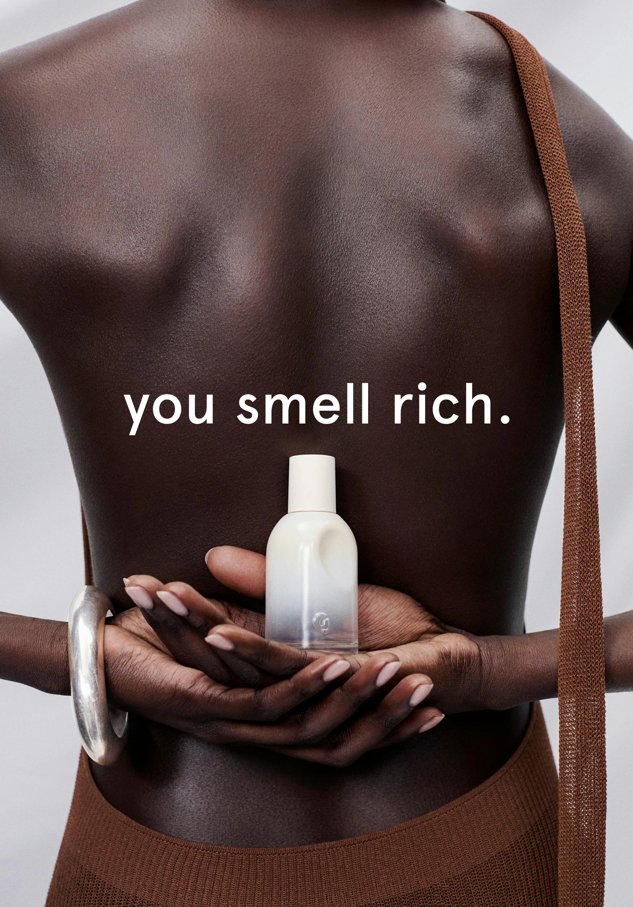 A dark torso with hands holding a white fragrance bottle, the words you smell rich across the image
